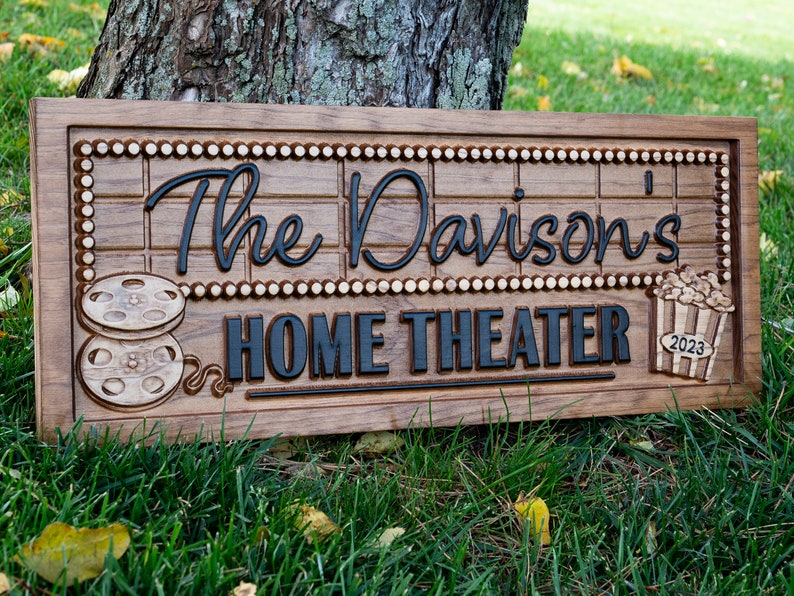 Pu&ograve; includere: Un cartello in legno con il testo "The Davison's Home Theater" in lettere nere. Il cartello &egrave; decorato con una bobina di pellicola e un secchiello di popcorn.