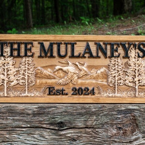 May include: A wooden sign with the text "The Mulaney's Est. 2024" carved into it. The sign features a carved image of two ducks flying over a mountain range with trees on either side.