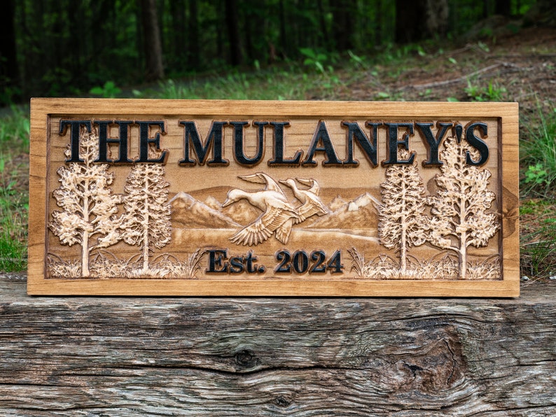 May include: A wooden sign with the text "The Mulaney's Est. 2024" carved into it. The sign features a carved image of two ducks flying over a mountain range with trees on either side.
