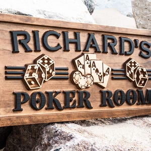 May include: A wooden sign with the text "Richard's Poker Room" in black lettering. The sign is decorated with carved images of playing cards, dice, and poker chips.