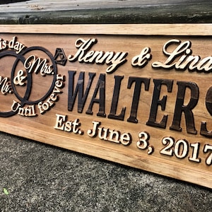 Pu&ograve; includere: Un cartello in legno con il testo "From this day Until forever Mr. & Mrs. Kenny & Linda WALTERS Est. June 3, 2017" e due anelli intrecciati con un diamante.