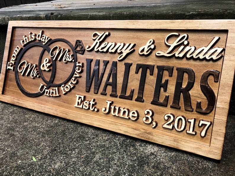 Pu&ograve; includere: Un cartello in legno con il testo "From this day Until forever Mr. & Mrs. Kenny & Linda WALTERS Est. June 3, 2017" e due anelli intrecciati con un diamante.