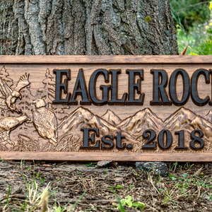 May include: A wooden sign with a carved design of eagles and mountains. The sign reads "Eagle Rock Est. 2018".