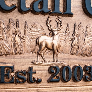 Peut inclure: Une pancarte en bois avec les mots "Est. 2003" grav&eacute;s dessus. La pancarte pr&eacute;sente &eacute;galement une image grav&eacute;e d'un cerf debout dans une for&ecirc;t.