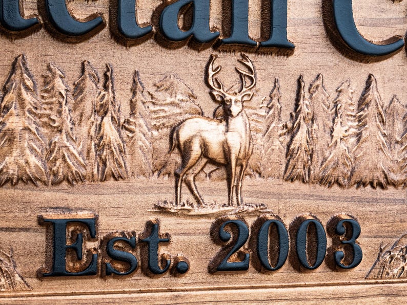 Peut inclure: Une pancarte en bois avec les mots "Est. 2003" grav&eacute;s dessus. La pancarte pr&eacute;sente &eacute;galement une image grav&eacute;e d'un cerf debout dans une for&ecirc;t.