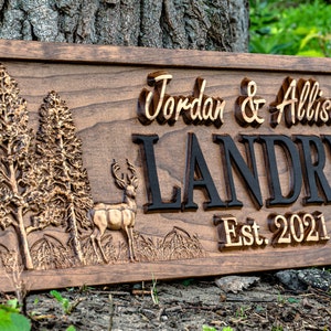 May include: A wooden sign with a carved deer, trees, and the text "Jordan & Allison Landry Est. 2021".