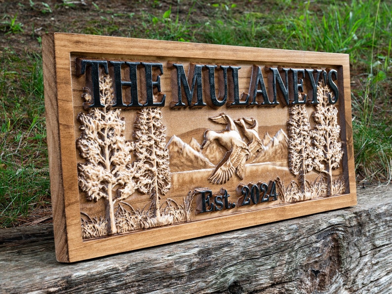 May include: A wooden sign with the text "The Mulaney's Est. 2024" carved into it. The sign features a carved image of two ducks flying over a mountain range with trees on either side.