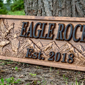 May include: A wooden sign with the text "Eagle Rock Est. 2018" carved into it. The sign features a carved image of two eagles and a mountain range.