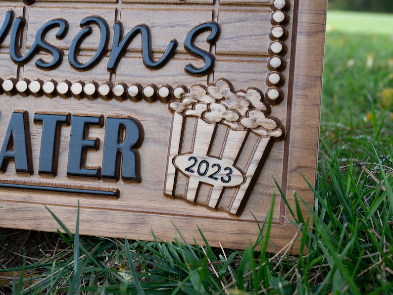 Pu&ograve; includere: Un cartello in legno con il testo "Wilson's Theater" e un secchiello di popcorn intagliato con l'anno "2023" sopra.