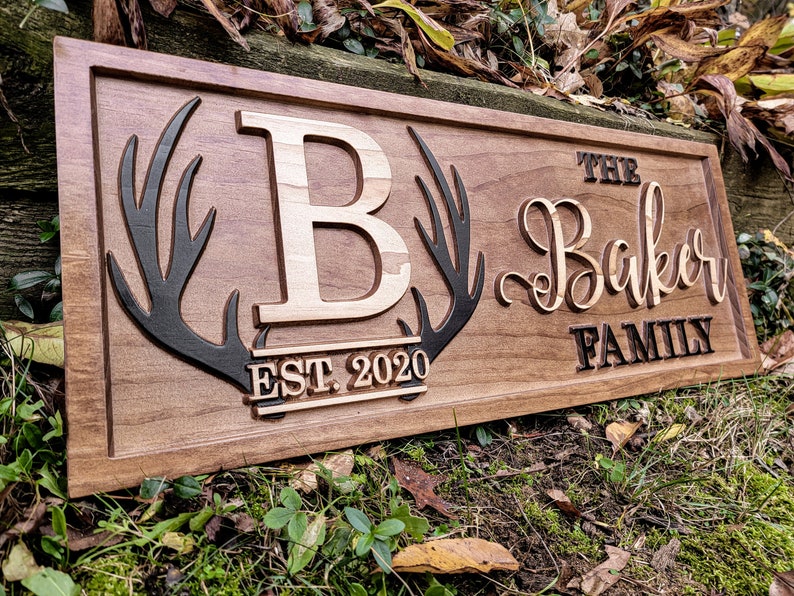 May include: A wooden sign with a carved 'B' and antlers, the text 'The Baker Family Est. 2020' is also carved into the sign.