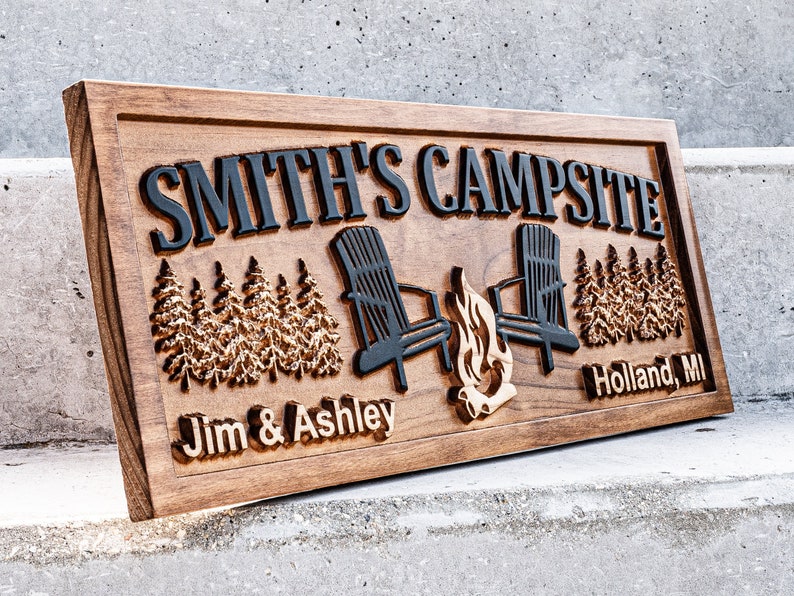 Puede incluir: Un letrero de madera con el texto "Smith's Campsite" en letras negras. El letrero tambi&eacute;n presenta una imagen tallada de dos sillas Adirondack, una fogata y pinos. Los textos "Jim & Ashley" y "Holland, MI" tambi&eacute;n est&aacute;n tallados en el letrero.