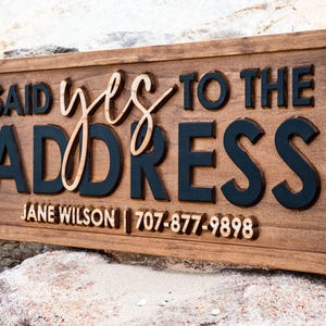 May include: A rectangular wooden sign with the words "SAID yes TO THE ADDRESS" in a layered design. The word "yes" is in a cursive font. The name "JANE WILSON" and a phone number are at the bottom.