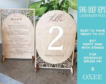 May include: Laser cut table number sign with a leafy design, the number 2, and the text "Anna + Alex". The sign is made of wood and is 5 inches by 7 inches. It is available in various thicknesses from 3 to 6 millimeters.