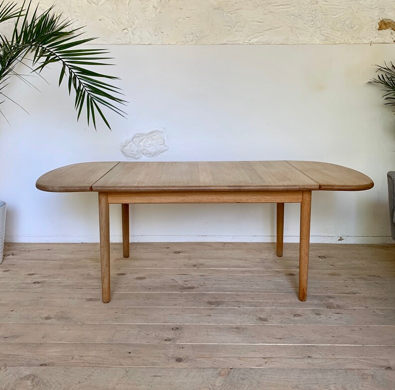 Puede incluir: Una mesa de comedor extensible de madera clara con una tapa rectangular redondeada y cuatro patas. La mesa est&aacute; hecha de madera maciza y tiene un acabado natural.