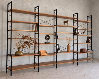 Op de afbeelding: Een grote modulaire stellingkast met verticale frames van zwart metaal en horizontale houten planken. De structuur bevat kruisverbindingen en bevat diverse decoratieve voorwerpen, waaronder boeken, vazen en sculpturen.