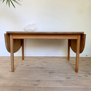 Puede incluir: Una mesa de madera con hojas abatibles de acabado marr&oacute;n claro. La mesa tiene dos hojas que se pueden extender para hacerla m&aacute;s grande. La mesa est&aacute; sobre un suelo de madera.