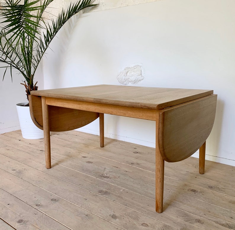 Puede incluir: Una mesa ovalada de madera clara con hojas abatibles y acabado natural. La mesa tiene cuatro patas y est&aacute; hecha de madera maciza. La mesa est&aacute; en una habitaci&oacute;n con suelo de madera clara.