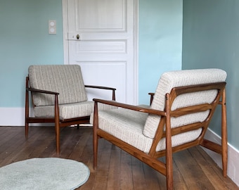 Op de afbeelding: Twee fauteuils met donkerbruine houten frames, taps toelopende poten en lichtgrijze, gestructureerde stoffen bekleding op de zit- en rugkussens. De stoelen hebben open armleuningen en een zichtbare houten constructie bij de rugleuning.