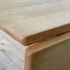 Puede incluir: Primer plano de una mesa de madera clara con un borde redondeado y una bisagra visible. La mesa est&aacute; hecha de madera natural con un patr&oacute;n de veta clara.