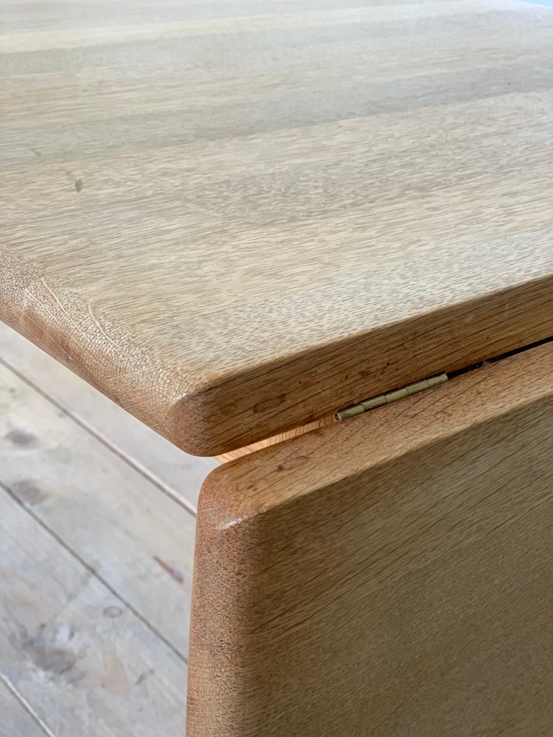 Puede incluir: Primer plano de una mesa de madera clara con un borde redondeado y una bisagra visible. La mesa est&aacute; hecha de madera natural con un patr&oacute;n de veta clara.