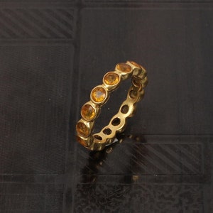 May include: A gold band ring with a row of round, orange gemstones.