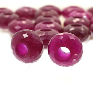 May include: Two faceted ruby red gemstone beads with a hole in the center. The beads are on a white surface.