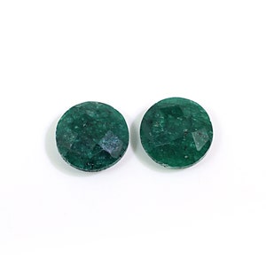 May include: Two round, green emerald gemstones with a faceted cut.