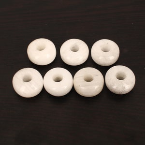 Puede incluir: Ocho cuentas blancas en forma de rosquilla con un agujero en el centro. Las cuentas están hechas de un material blanco liso y tienen una superficie ligeramente texturizada.