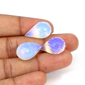 May include: Three pear-shaped, faceted opalescent gemstones. The gems have a milky white base with iridescent blue and yellow hues. The facets create a sparkling effect, and the stones are displayed against a neutral background.