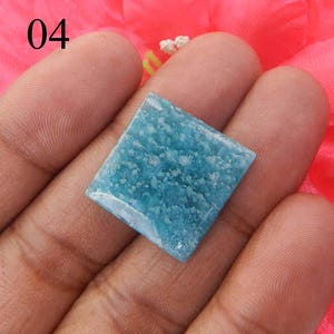 Puede incluir: Una piedra preciosa cuadrada de color azul claro con un patr&oacute;n moteado. La piedra preciosa se sostiene en una mano.
