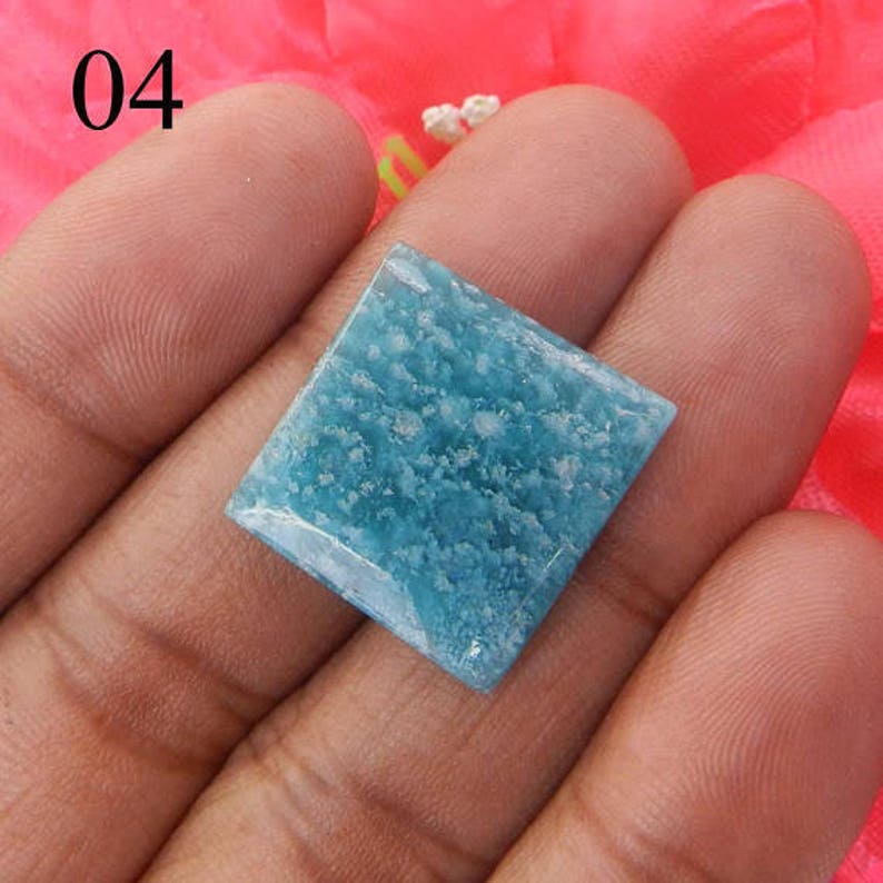 Puede incluir: Una piedra preciosa cuadrada de color azul claro con un patr&oacute;n moteado. La piedra preciosa se sostiene en una mano.