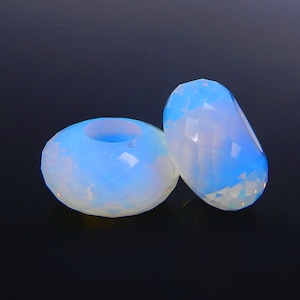 May include: Two iridescent opal beads with a faceted design. The beads are a light blue color with a white opalescent sheen.