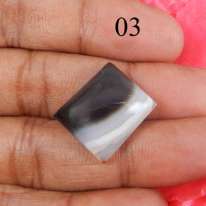 May include: A white and black agate cabochon with a square shape. The stone has a swirling pattern of white and black.