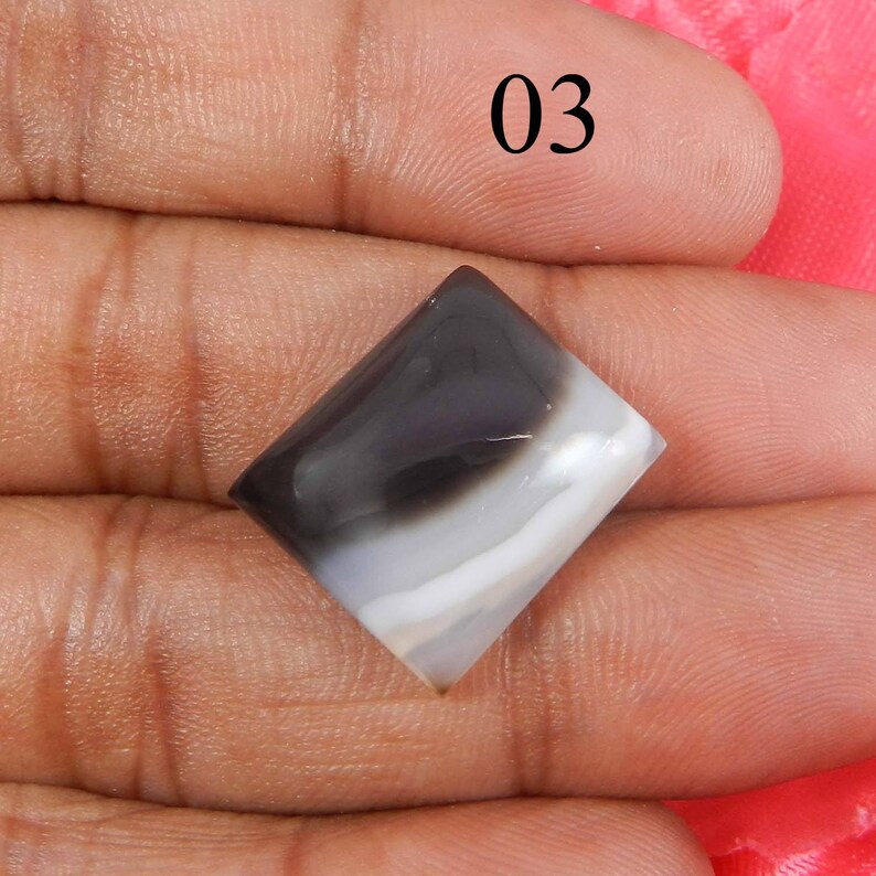 May include: A white and black agate cabochon with a square shape. The stone has a swirling pattern of white and black.