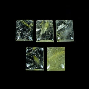 Pode incluir: Cinco cabochões retangulares de quartzo transparente com inclusões de rutilo dourado. Os cabochões são facetados e têm um acabamento liso e polido.