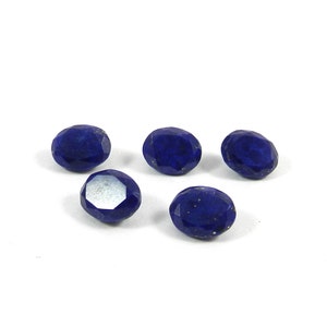 Puede incluir: Cinco piedras preciosas de lapislázuli de forma ovalada, de color azul oscuro y con destellos dorados. Las piedras están facetadas y tienen un acabado pulido.