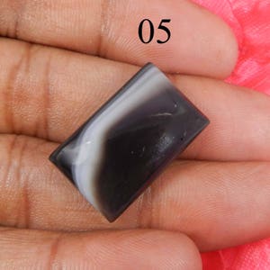 May include: A black and white agate cabochon with a rectangular shape. The stone has a swirling pattern of black and white.