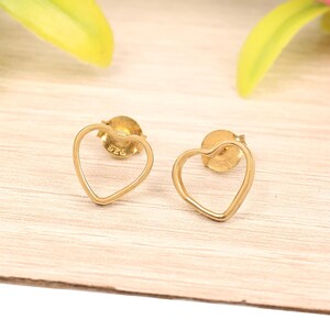 May include: A pair of gold heart-shaped earrings with a hollow center. The earrings are made of metal and have a post back.