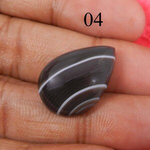 May include: A black and white banded agate cabochon with a teardrop shape. The stone has a smooth, polished surface.