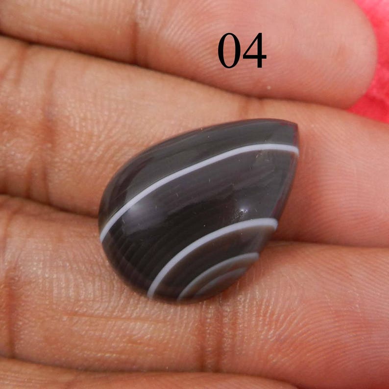 May include: A black and white banded agate cabochon with a teardrop shape. The stone has a smooth, polished surface.