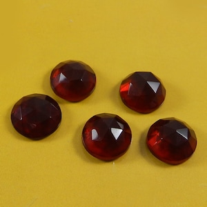 May include: Five red, faceted glass gems on a yellow background. The gems are round and have a slightly domed shape.