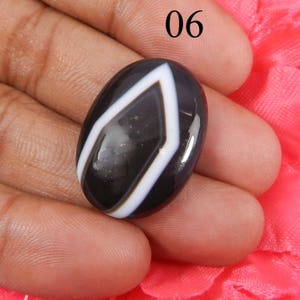 May include: Black and white agate gemstone cabochon with a diamond pattern. The gemstone is oval shaped and has a glossy finish.