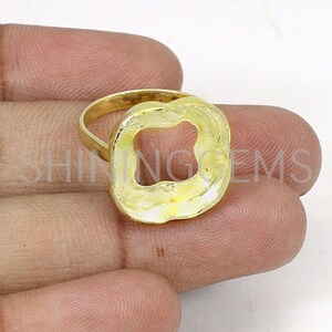May include: Gold ring with a square-shaped cutout in the center. The ring is thick and has a textured surface.