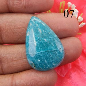 Puede incluir: Una piedra preciosa de color azul claro en forma de l&aacute;grima con un patr&oacute;n de m&aacute;rmol verde y blanco. La piedra preciosa es lisa y pulida.