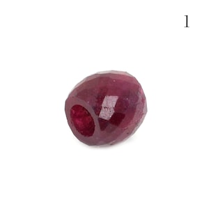 May include: A deep red faceted gemstone bead. The bead is round and has a smooth, polished surface.