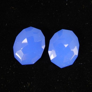 Peut inclure: Deux pierres précieuses ovales de couleur bleu clair avec une taille facetée. Les pierres précieuses sont posées sur un fond noir.