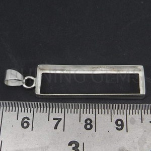May include: Silver pendant bezel setting for a rectangular stone. The bezel is 2.5 cm long and 1 cm wide. The pendant has a bail for attaching a chain.