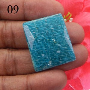 Puede incluir: Una piedra preciosa de amazonita cuadrada, de color azul claro, con una superficie lisa y pulida. La piedra tiene un patr&oacute;n estriado &uacute;nico e inclusiones blancas.