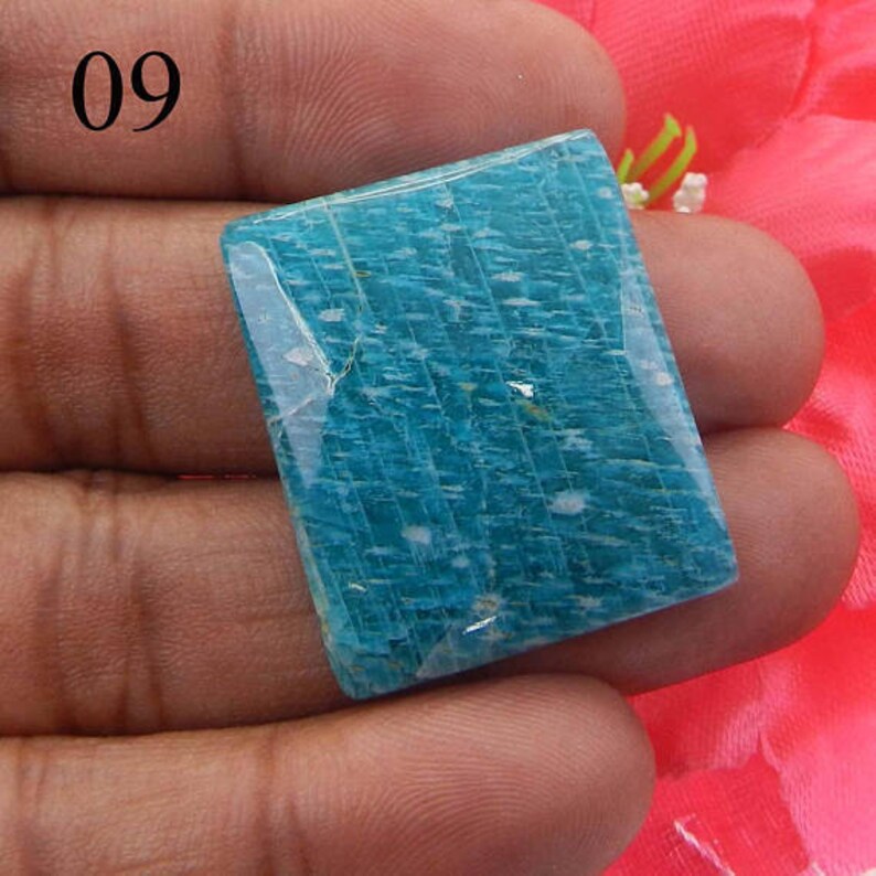 Puede incluir: Una piedra preciosa de amazonita cuadrada, de color azul claro, con una superficie lisa y pulida. La piedra tiene un patr&oacute;n estriado &uacute;nico e inclusiones blancas.