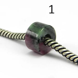 May include: A green and pink gemstone bead with a hole in the centre, threaded on a silver chain. The bead is a cylinder shape and has a mottled appearance.